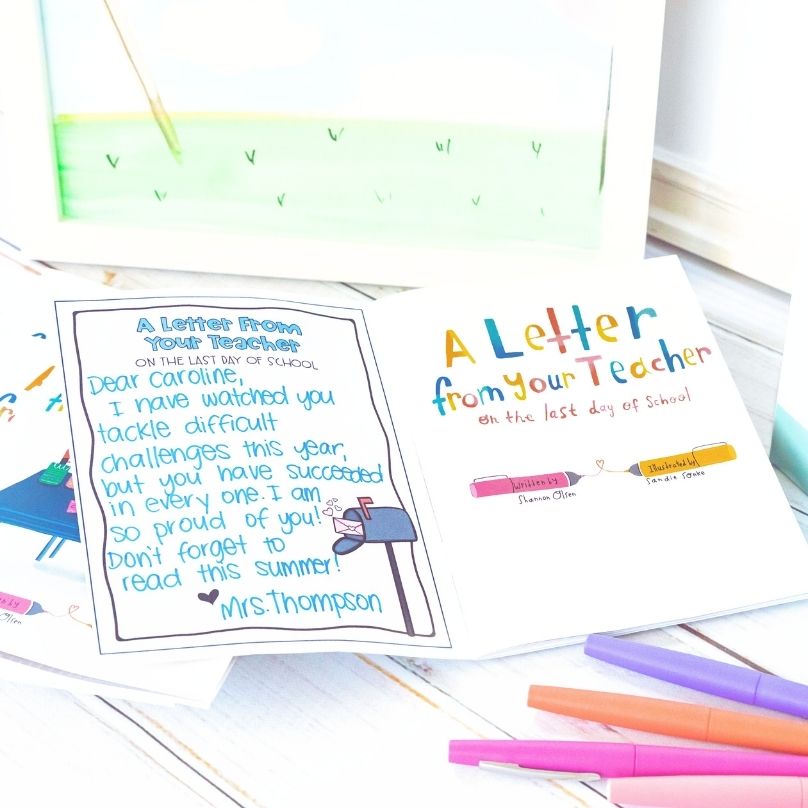 A colorful card reads “A Letter from your Teacher on the last day of school.” An open page shows a handwritten note to Caroline praising her hard work. Colorful pens and a framed drawing are on the white table beside it.
