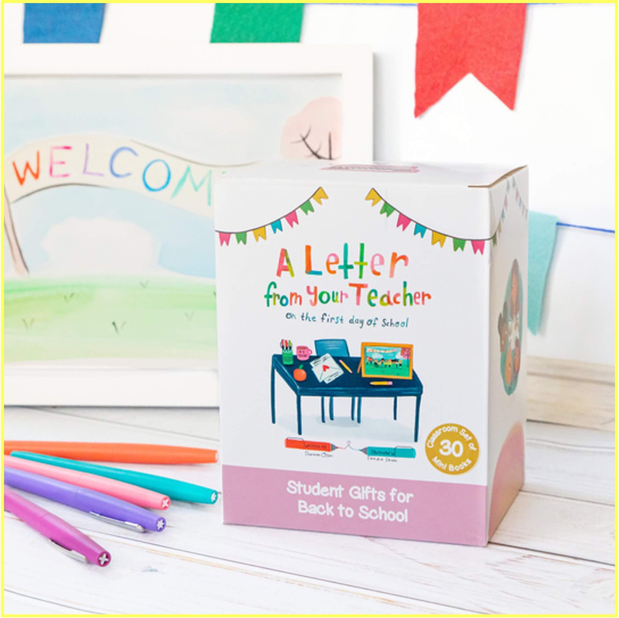A colorful box labeled A Letter from Your Teacher on the First Day of School sits on a desk with pens nearby and a WELCOME sign in the background. The box advertises student gifts for back to school.
