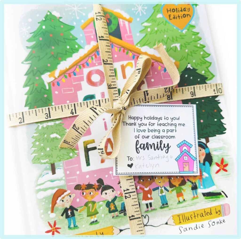 A childrens book wrapped with a measuring tape and a tag that reads: Happy holidays to you! Thank you for teaching me. I love being a part of our classroom family. Illustrated festive scene on the book cover.