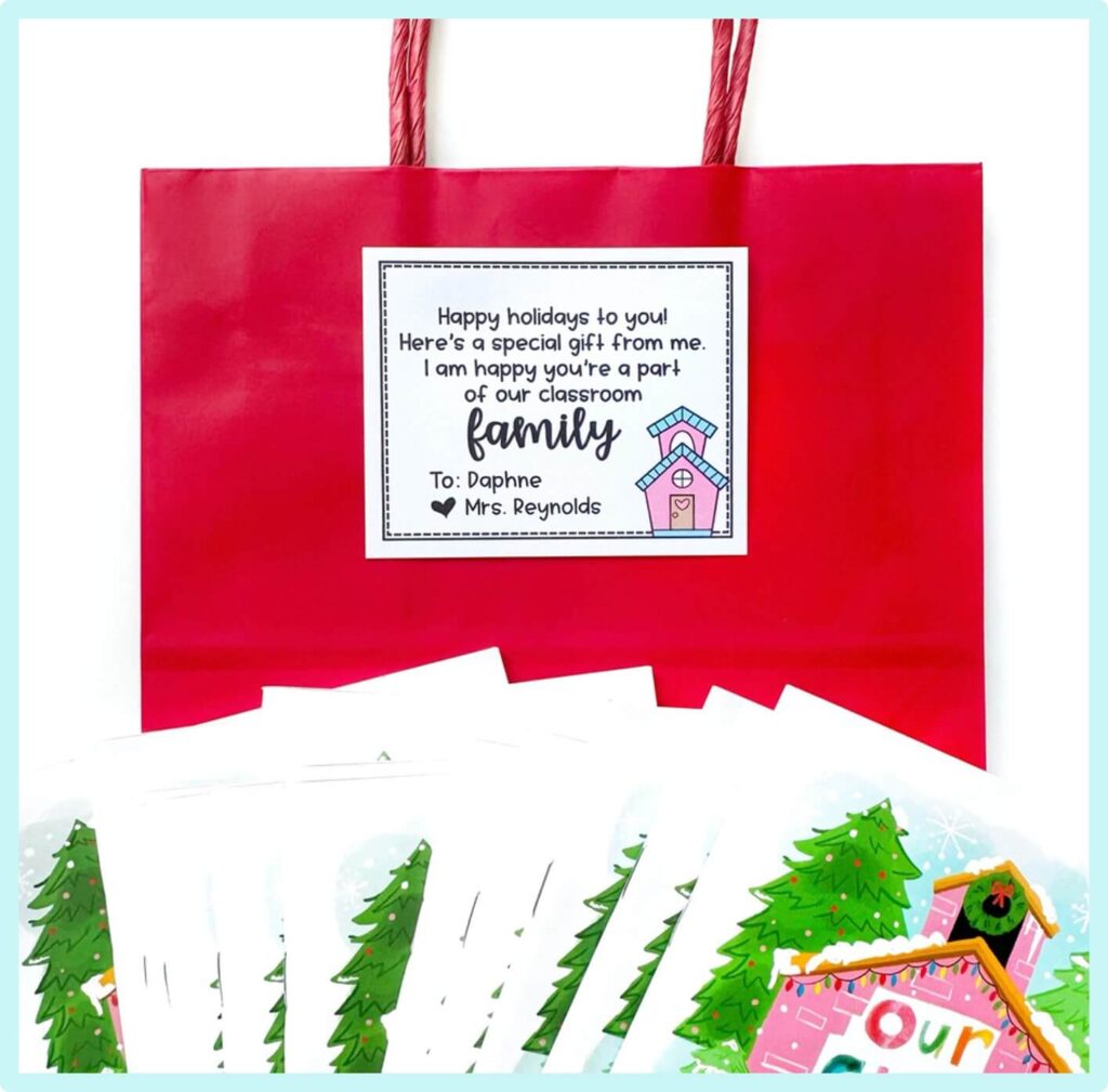 A red gift bag with a holiday card reading, Happy holidays to you! Heres a special gift from me. I am happy youre a part of our classroom family. Several colorful holiday cards are spread in front.